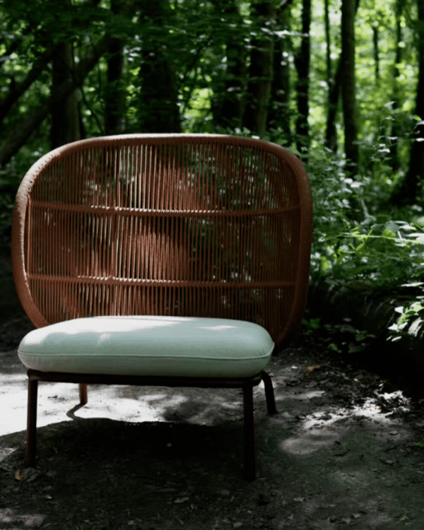 Kodo Cocoon lounge chair by Vincent Sheppard with striped and textured cushions, paired with an Olaf pouffe in matching striped fabric, set in a woodland garden.