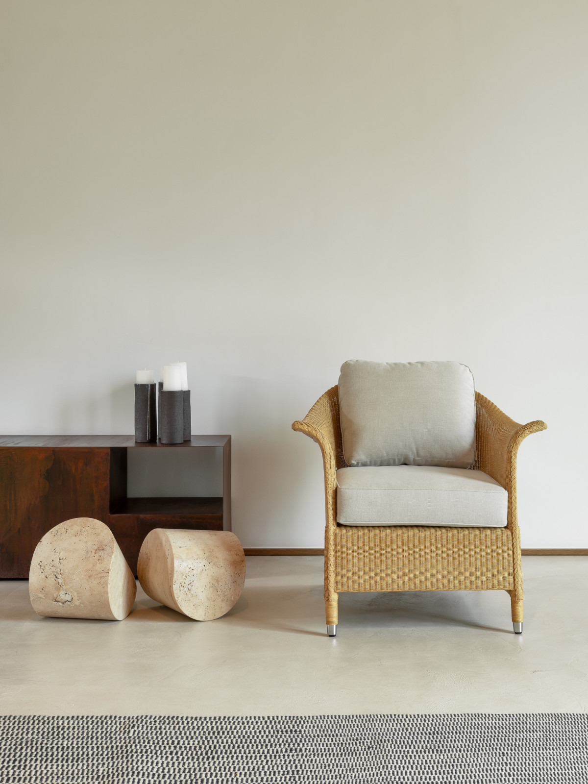 Victor Lounge-Sessel von Vincent Sheppard mit einem beigen Kissen, neben einem Holz-Beistelltisch und zwei Steinhockern auf einem minimalistischen Boden.