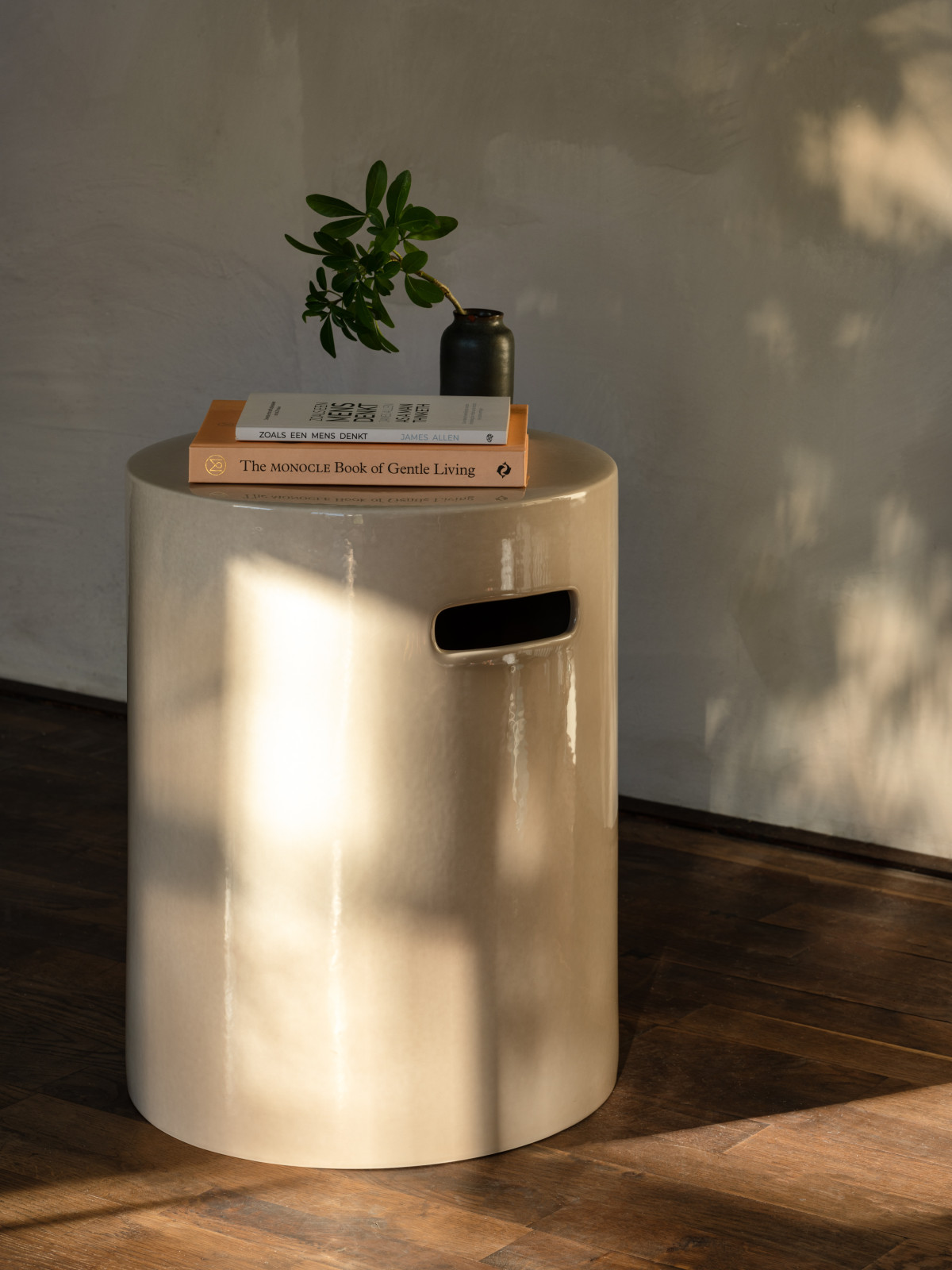 Vincent Sheppard Arvin Hocker in Keramik Mushroom mit glänzendem, zylindrischem Design und integrierten Griffen, dekoriert mit Büchern und einer kleinen Vase auf einem Holzboden.