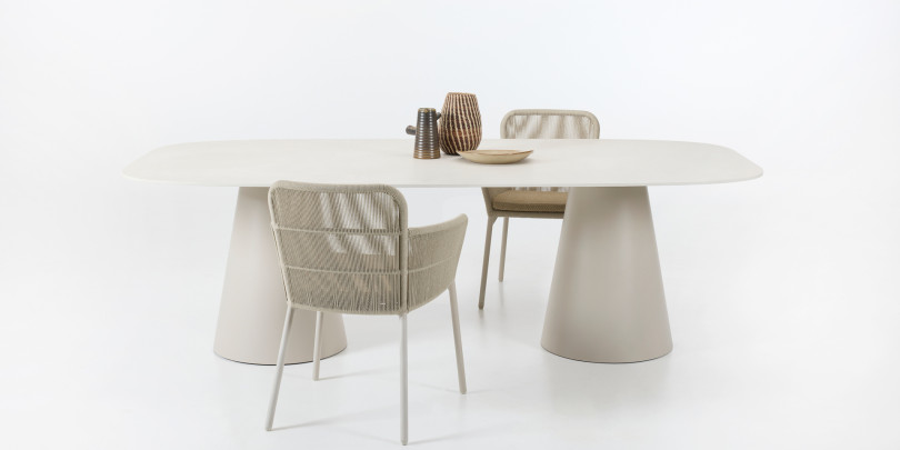 Chaises de salle à manger Akari de Vincent Sheppard avec assise tressée et structure métallique, associées à la table Sandro avec un plateau arrondi et deux pieds coniques dans une finition neutre.