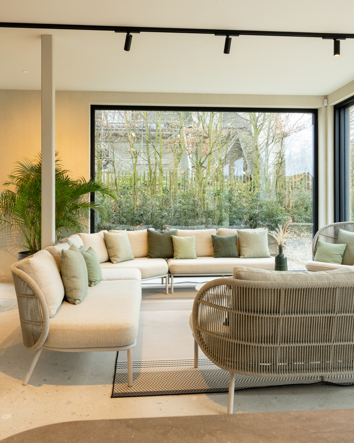 Vincent Sheppard Showroom mit dem modularen Kodo Sofa in neutralen Farbtönen, ausgestattet mit grünen und beigen Kissen, in einem hellen Raum mit bodentiefen Fenstern und Gartenblick.