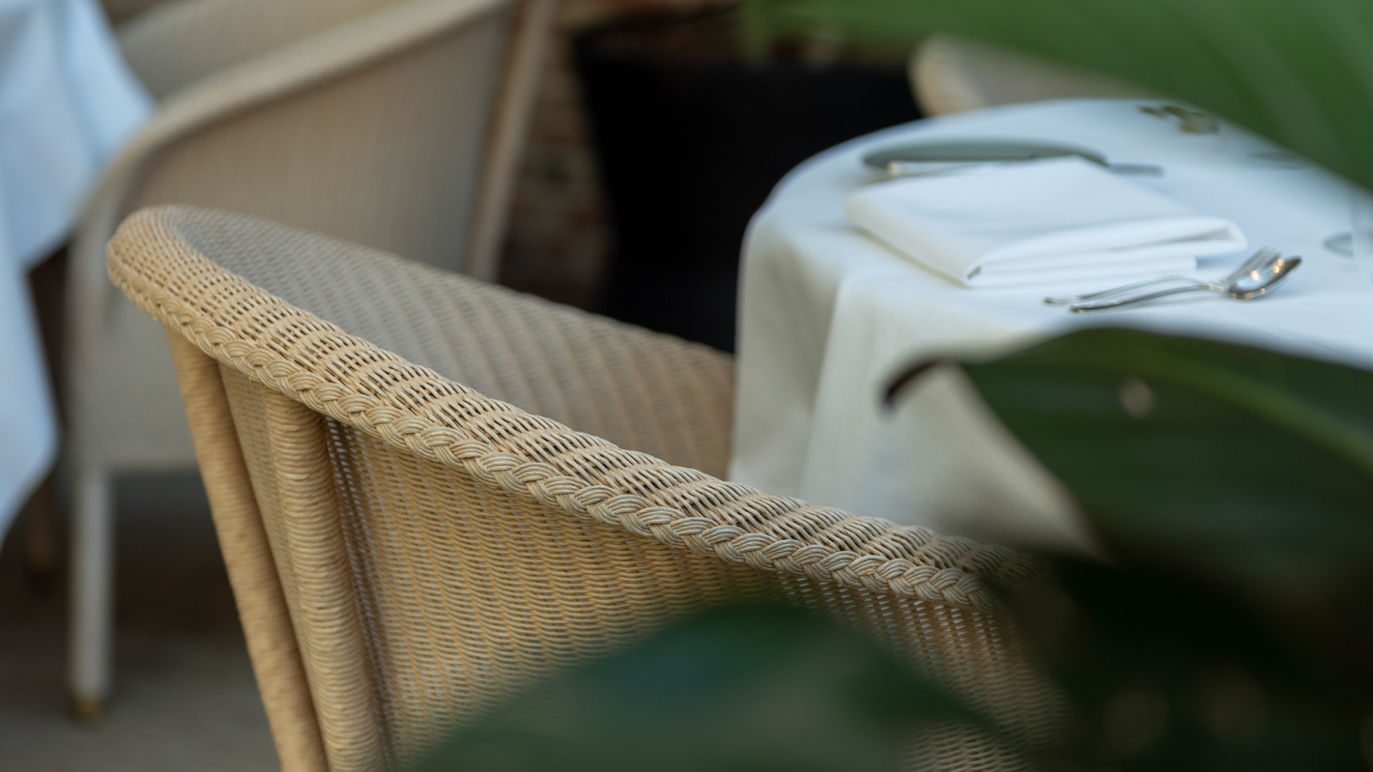 Restaurantterrasse mit Lloyd Loom-Stühlen und gedecktem Tisch mit weißem Tischtuch