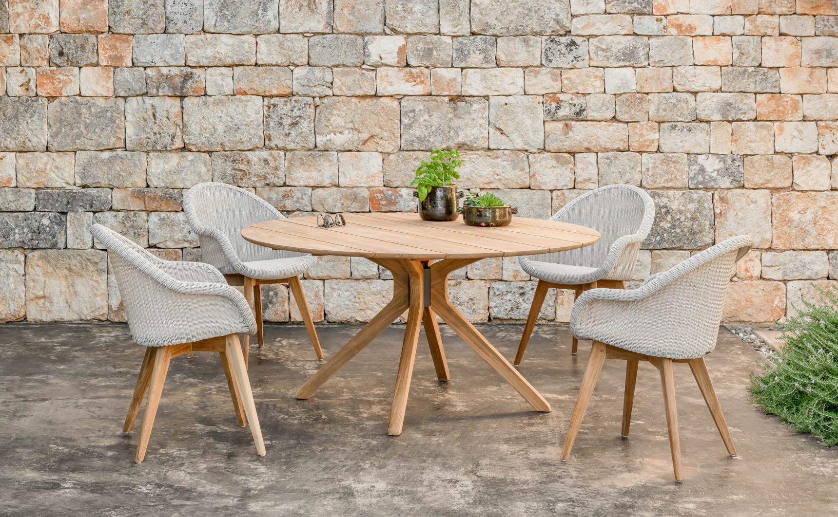Vincent Sheppard Noa dining table and Edgard dining chairs with teak base by a stone wall outdoors